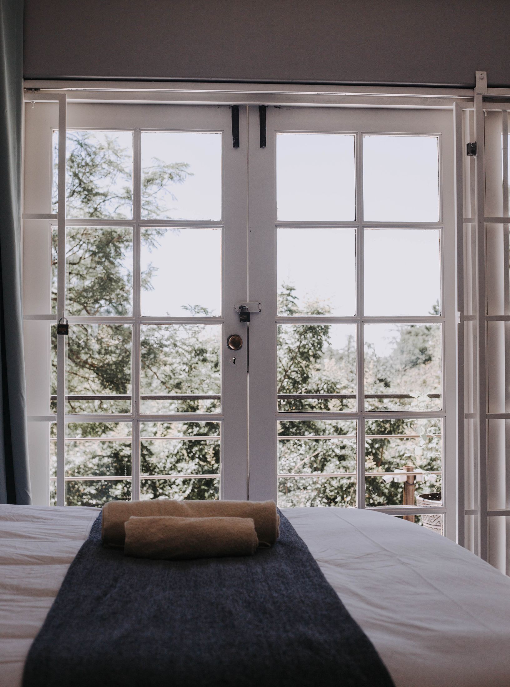 A made bed with a rolled towel, looking out through glass doors to the garden