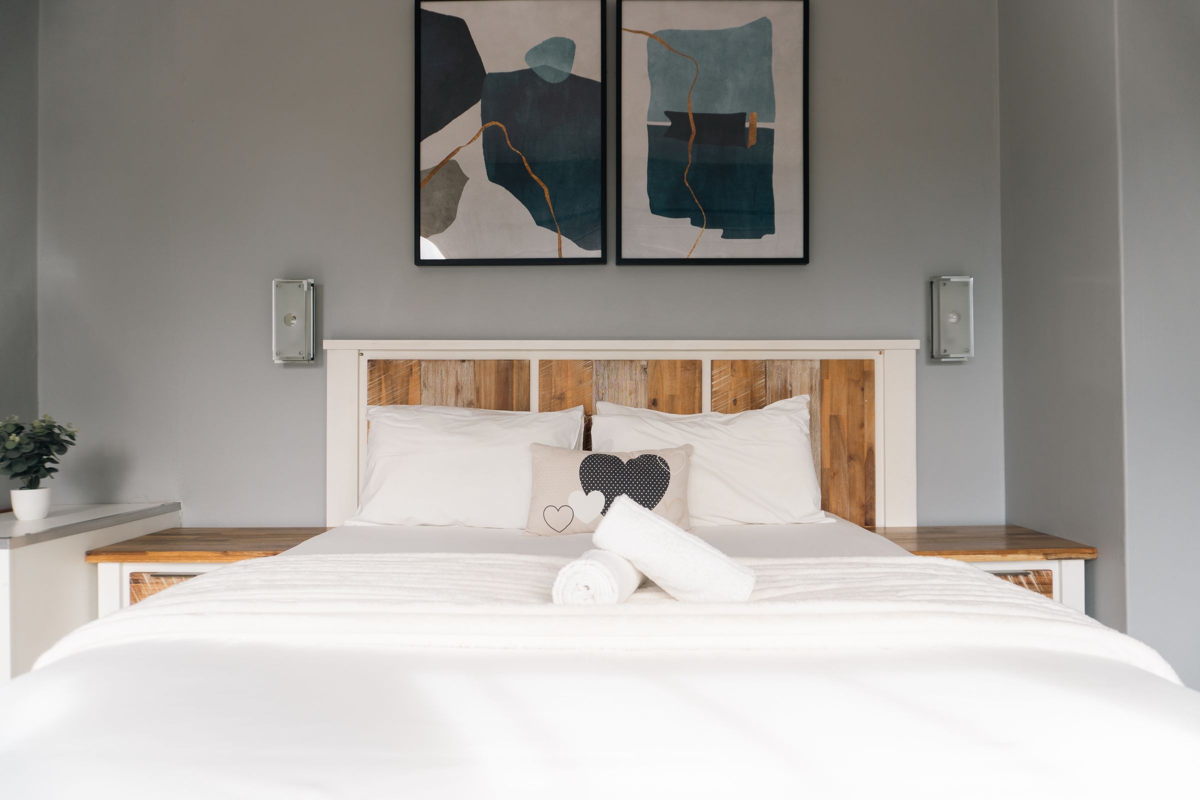 A bed with a heart cushion under two blue abstract prints