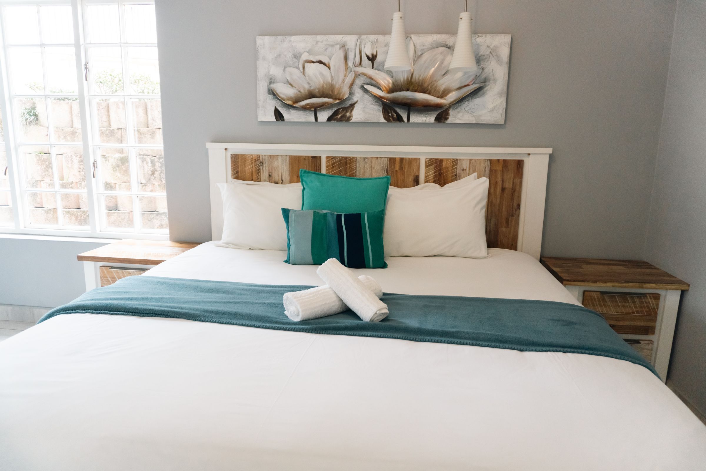 A bedroom with a timber headboard, teal cushions and rolled towels
