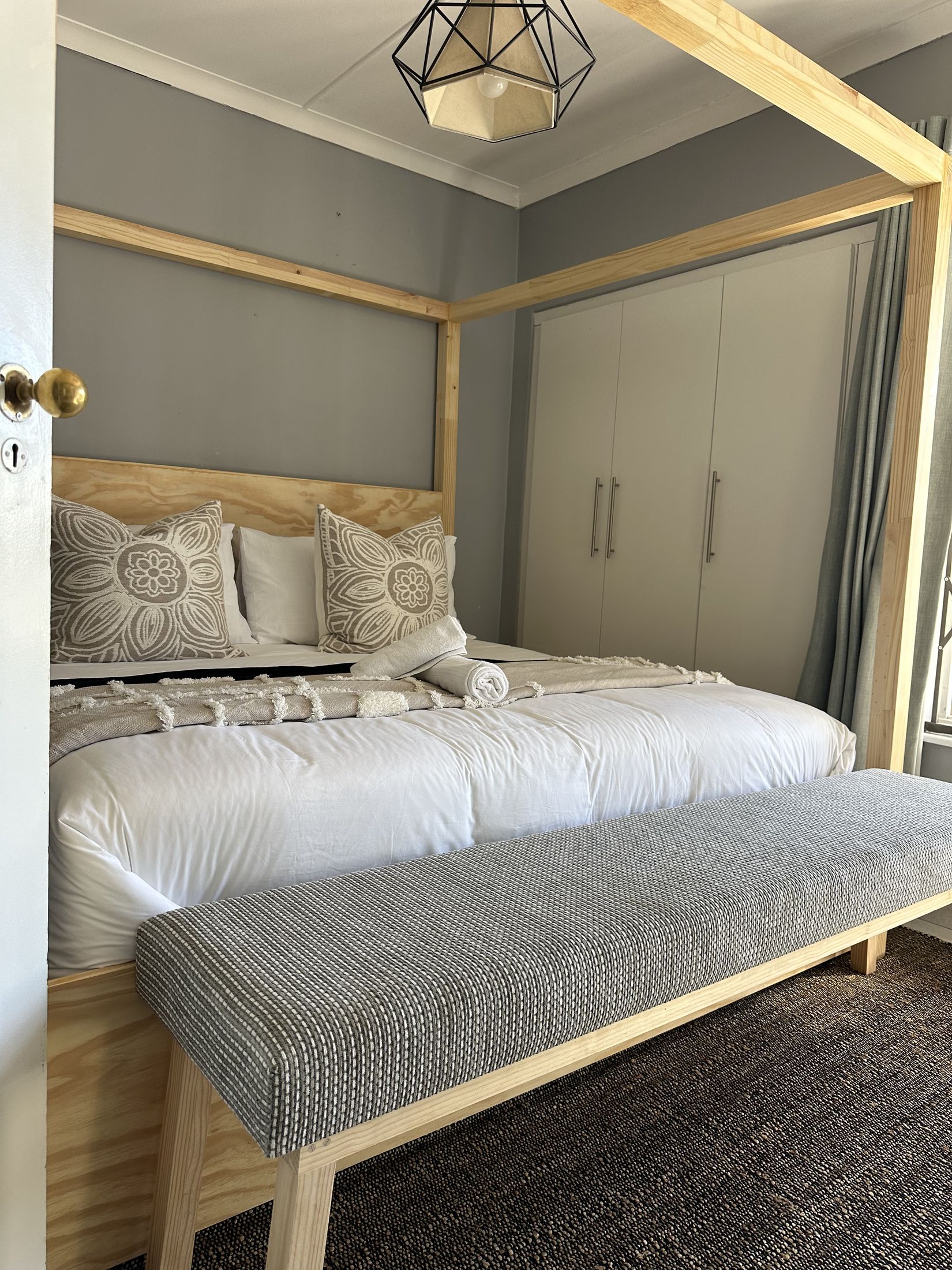 A four poster bed with a bench at its foot and cupboards behind