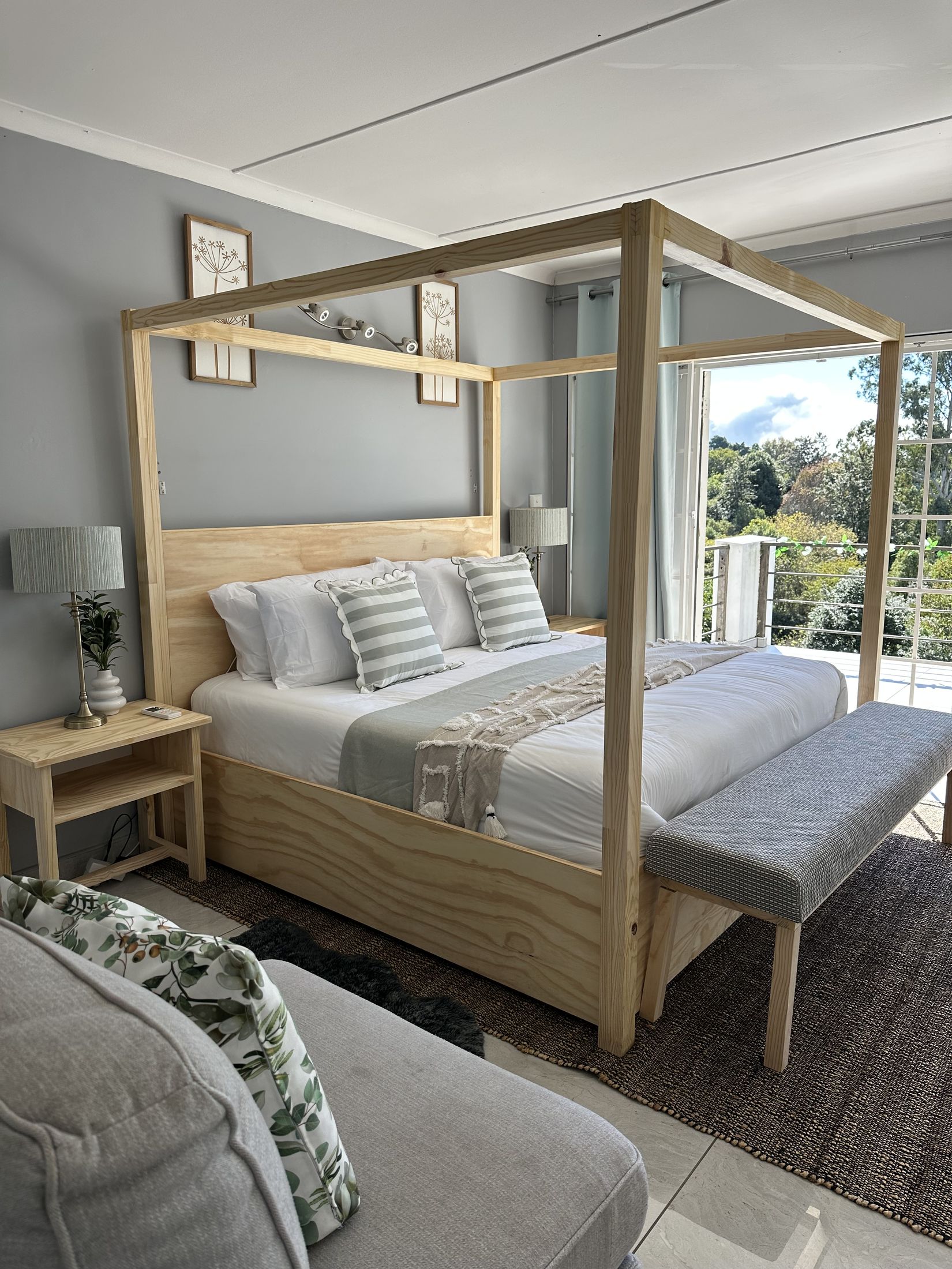 A four poster bed with striped cushions beside a balcony door