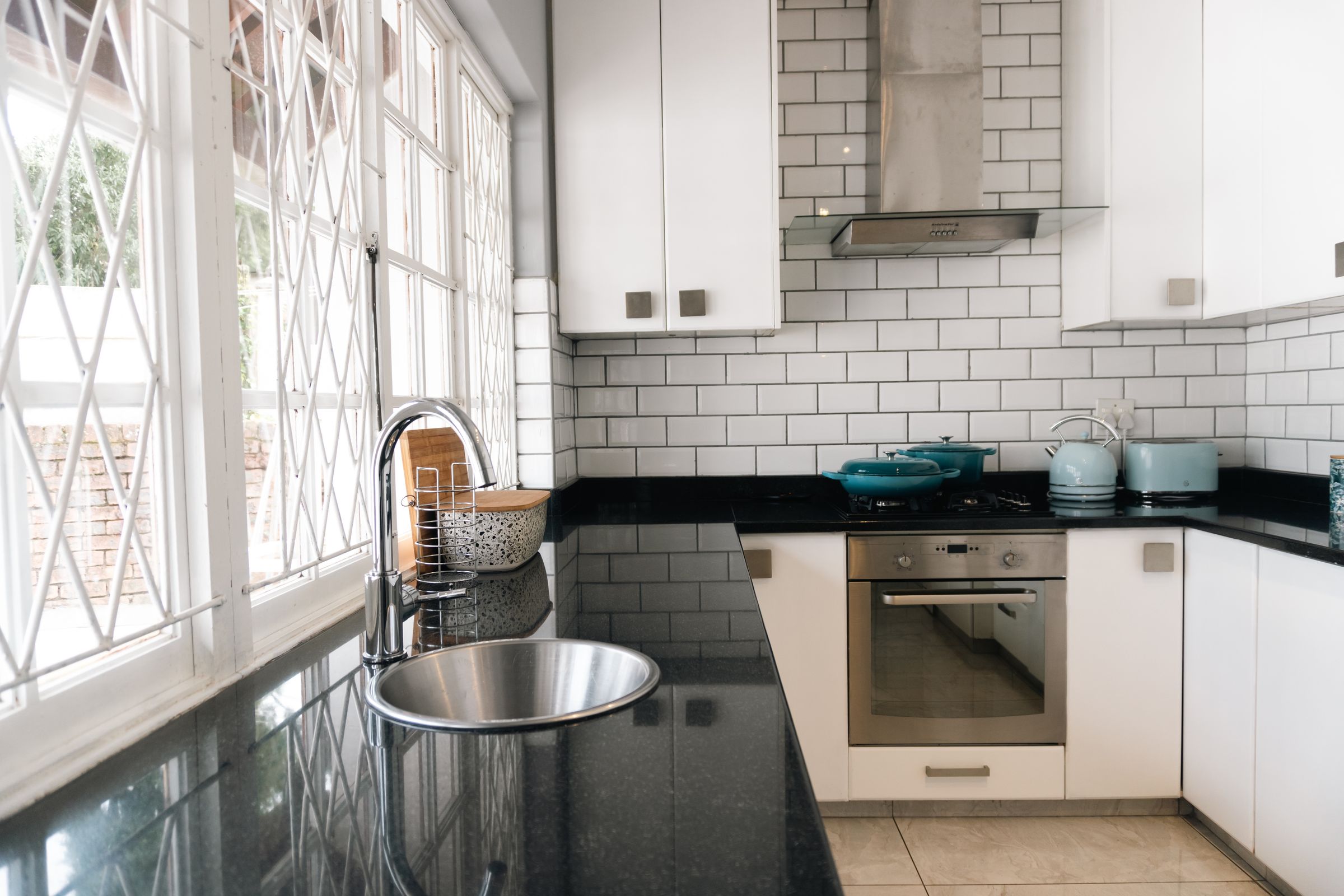 The kitchen sink under tall windows, with teal pots on the stove
