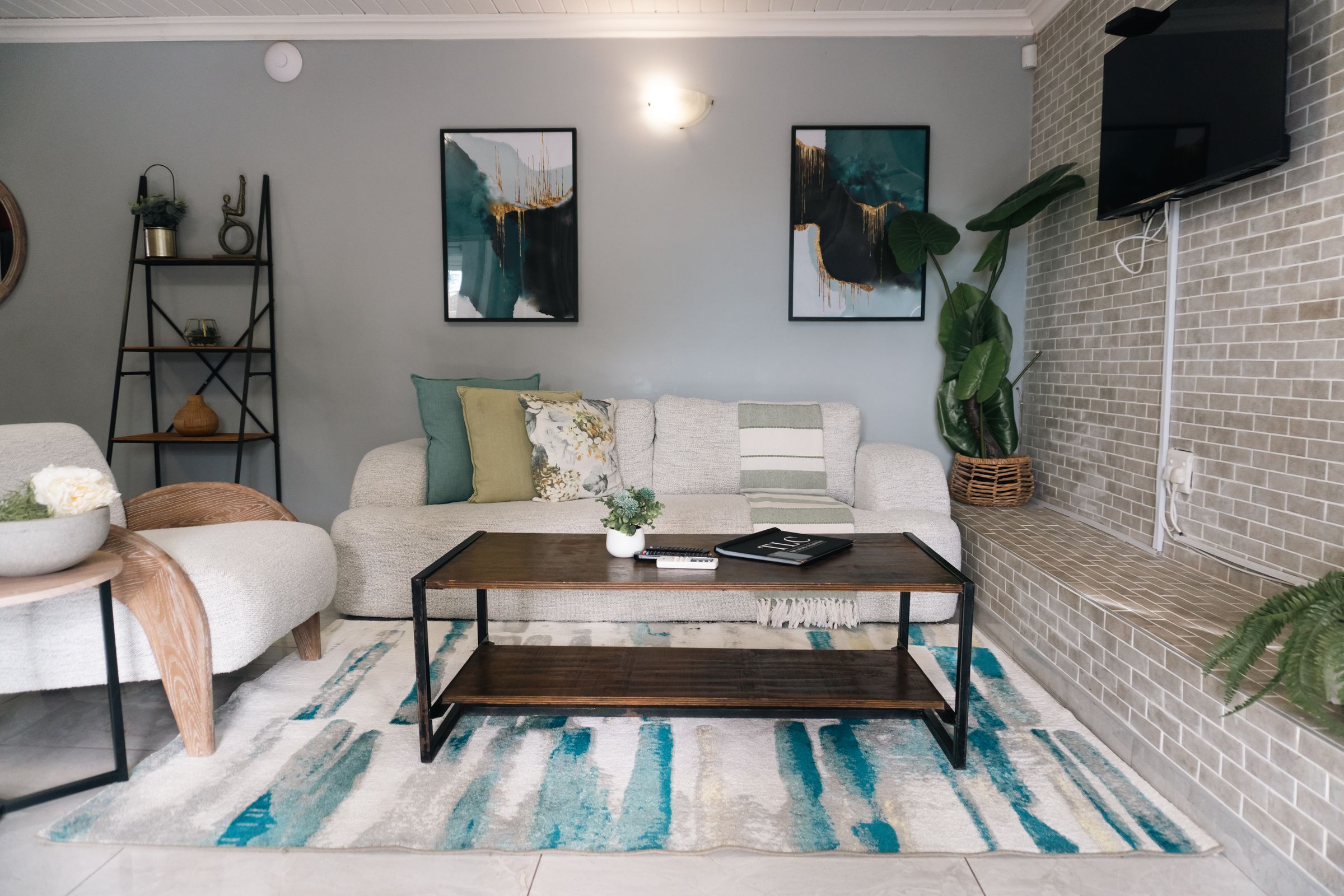 The villa lounge with a white couch, teal prints and a painted brick wall