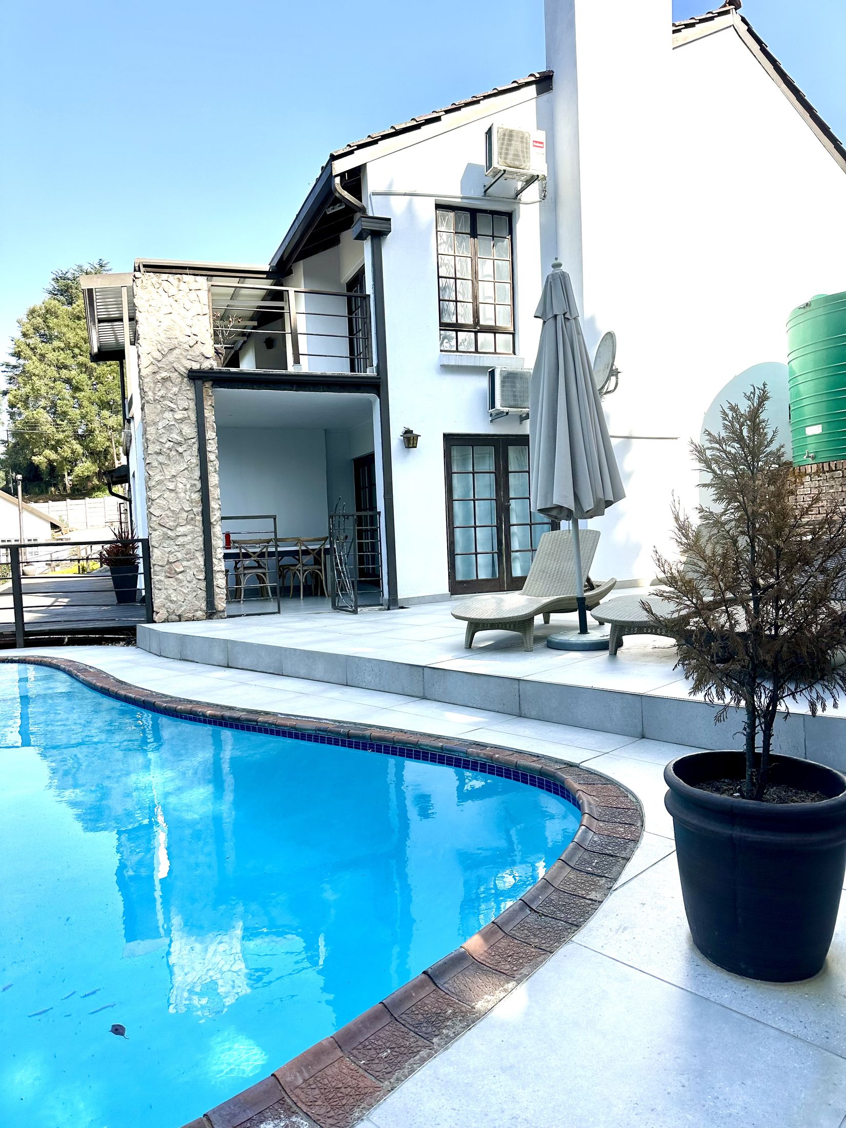 The pool curving past the back of the villa, with loungers and an umbrella