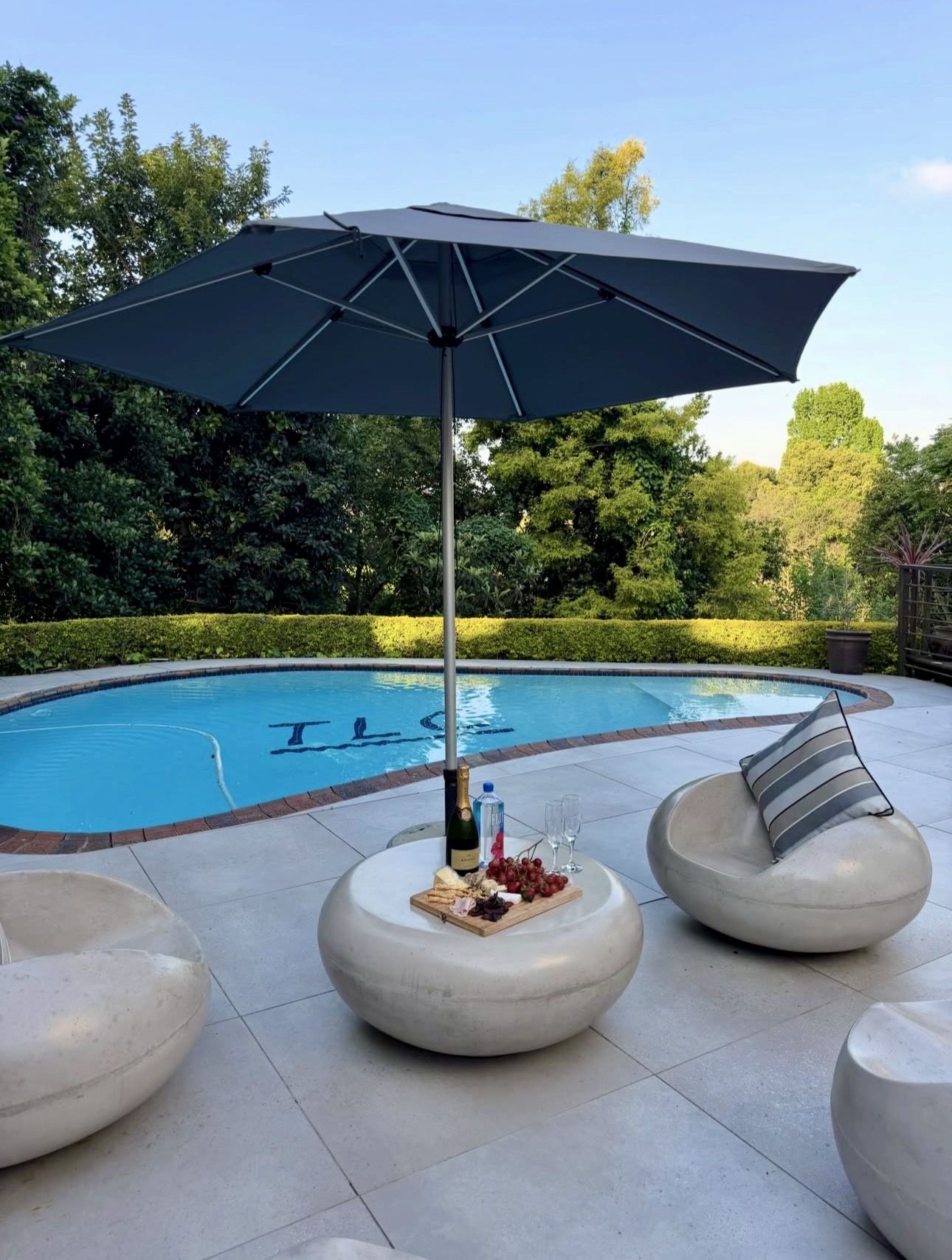 Stone seats and an umbrella beside the pool, with the TLC logo in its tiles