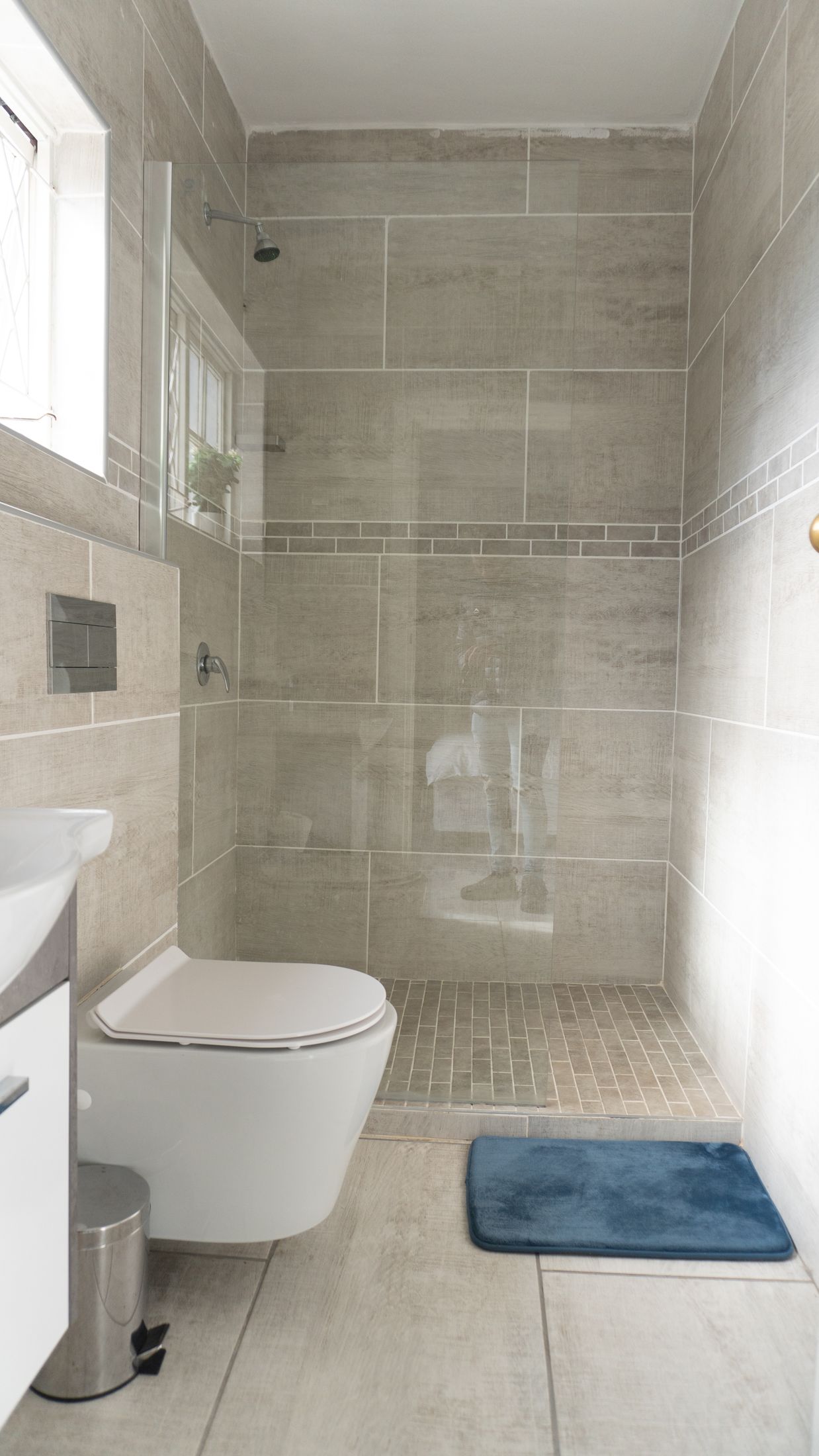 A walk in shower with grey tiles beside a wall hung toilet