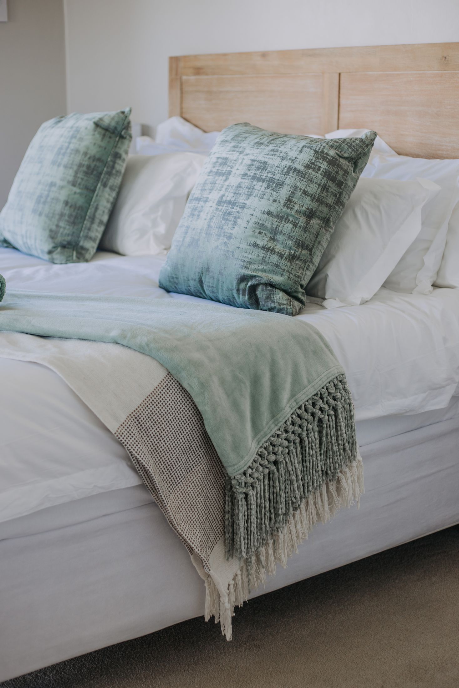 A bed with green cushions and a woven throw