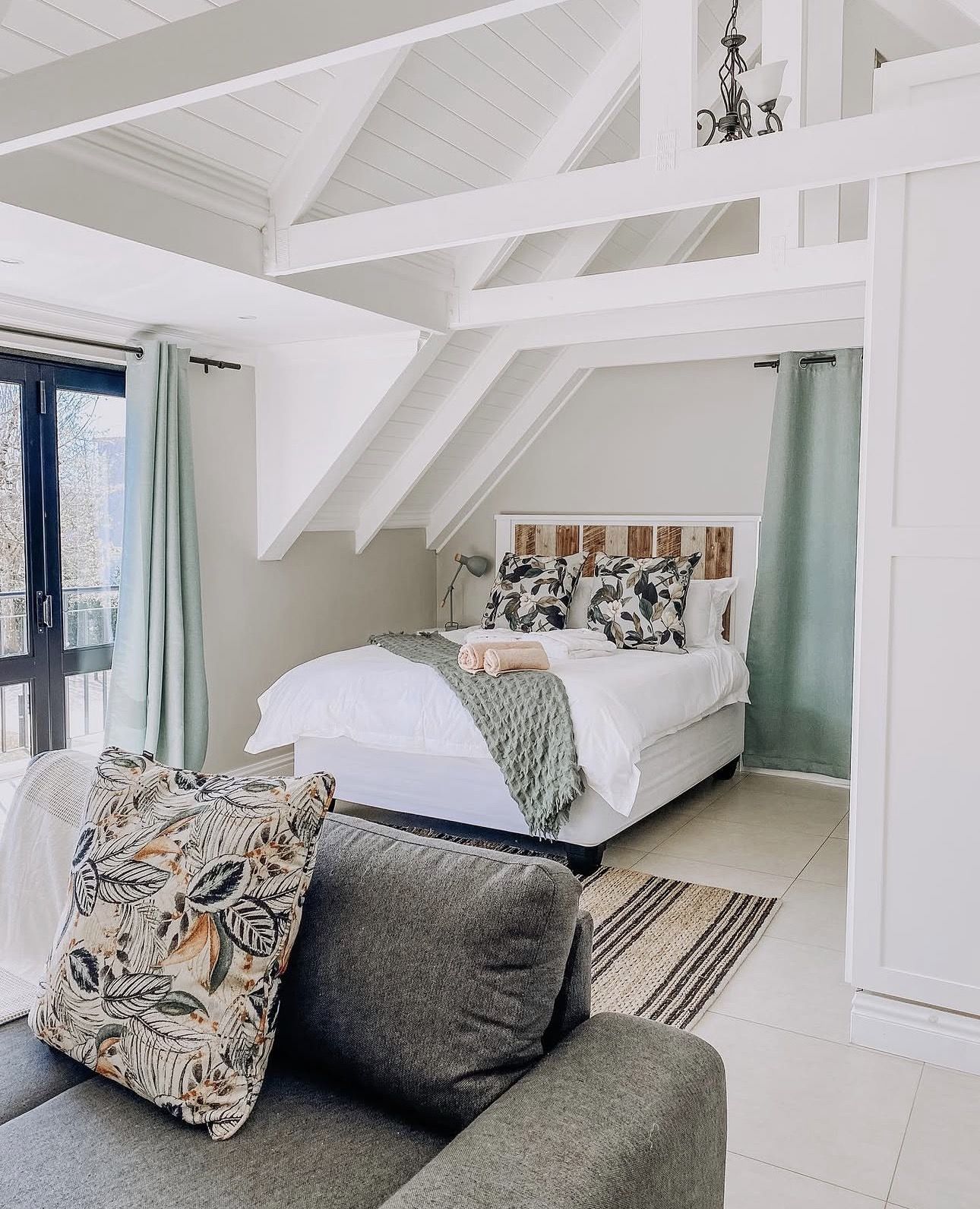 The loft bed under white roof trusses, seen past the grey couch