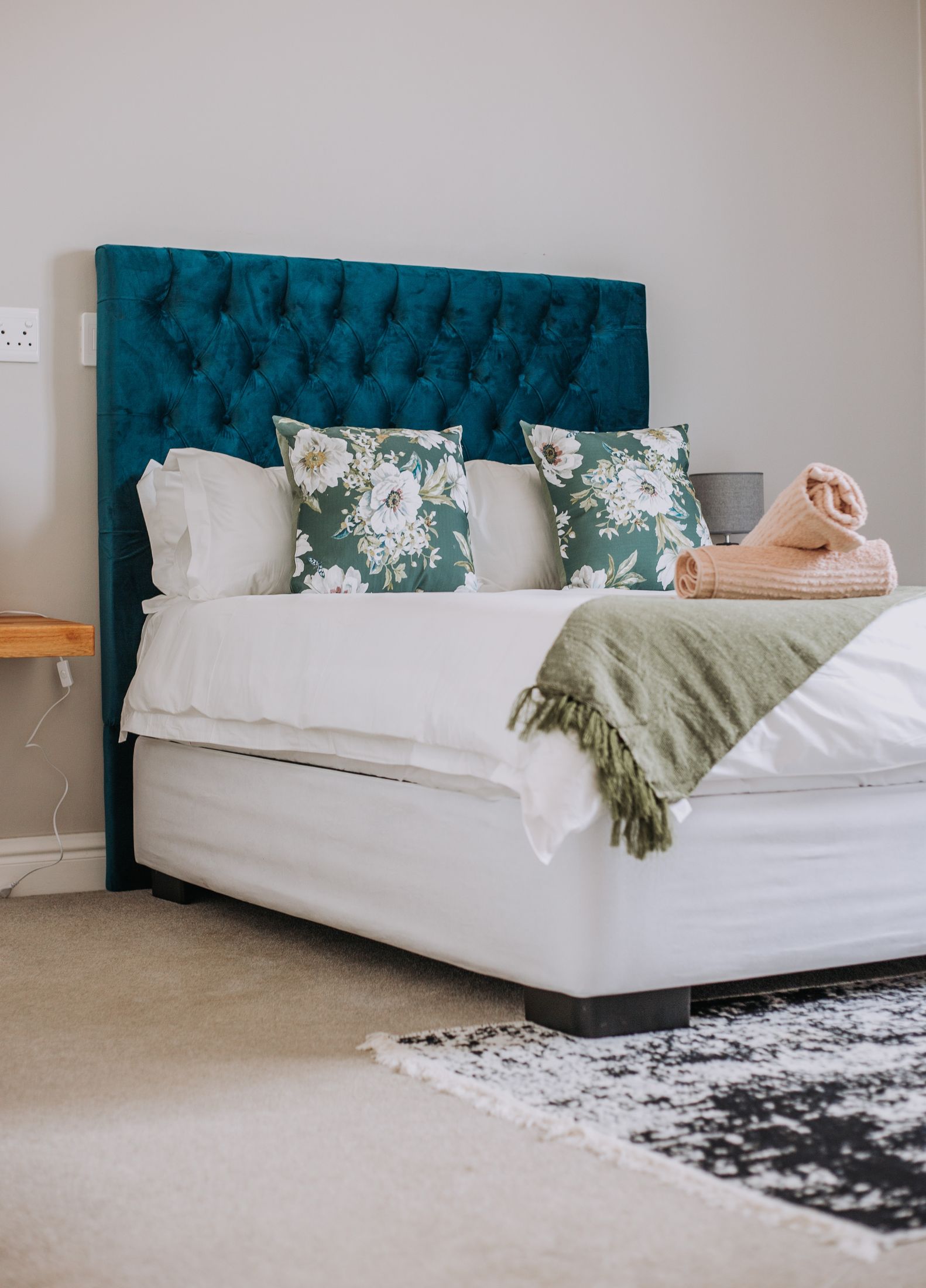 A bed with a deep teal buttoned headboard
