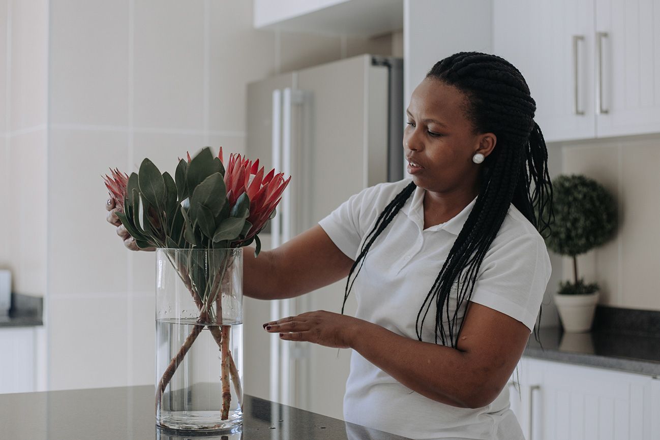 A housekeeper putting fresh proteas in a vase in the kitchen