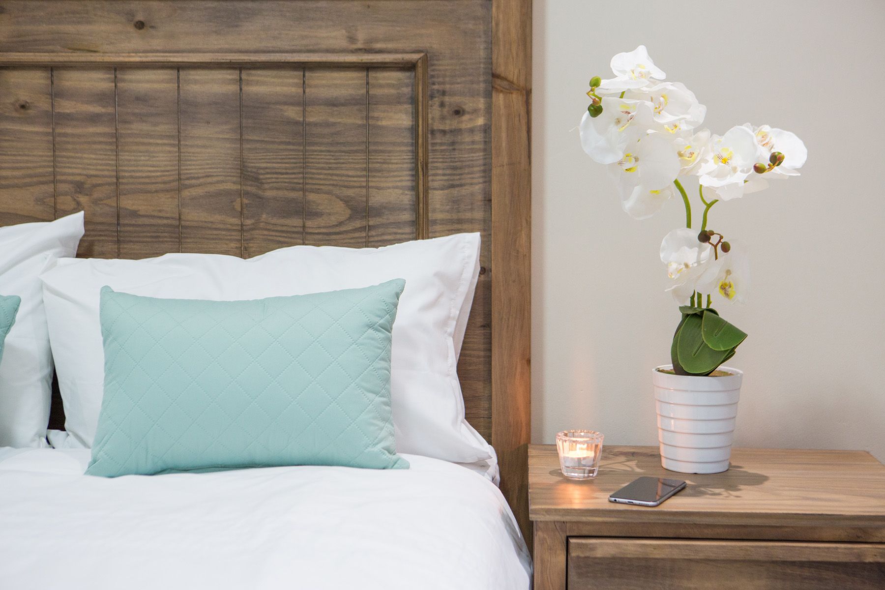 White linen, a teal cushion and an orchid beside a Unit 5 bed