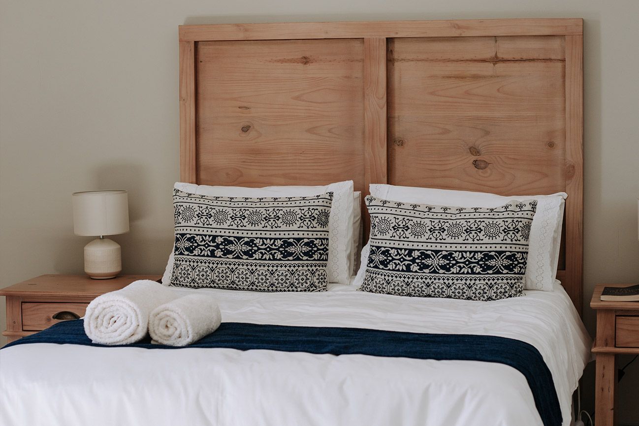 A double bed with a timber headboard and patterned cushions