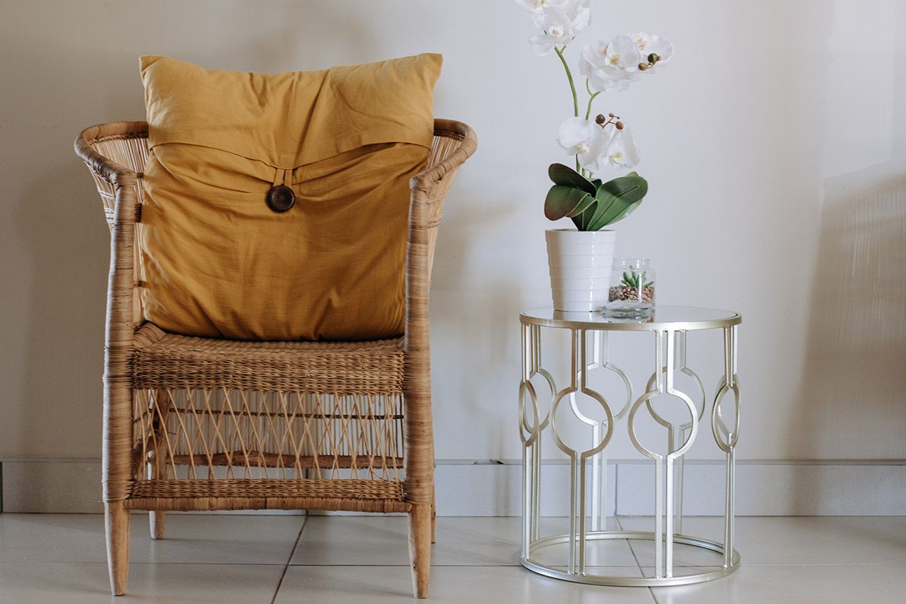 A woven chair with a mustard cushion next to a side table