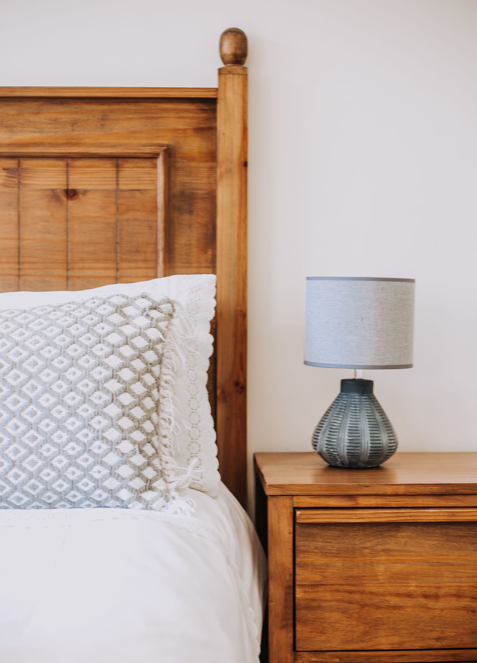 A bed with a timber headboard and a grey lamp on the bedside table