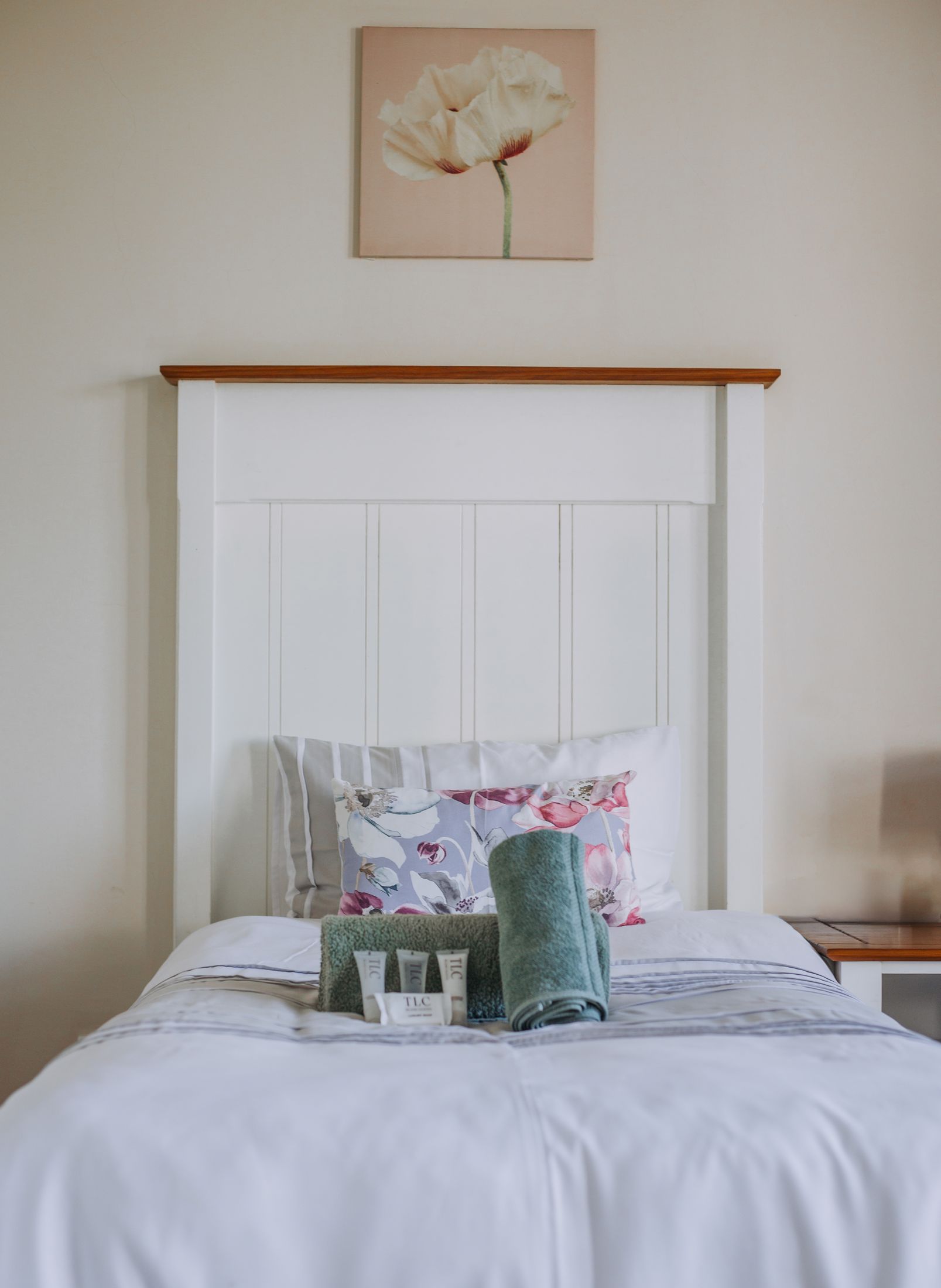 A bed with a white headboard, made up with towels and floral cushions