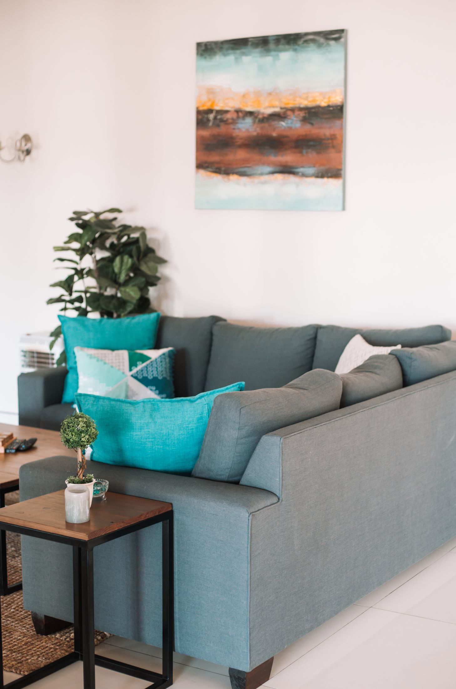A grey couch with teal cushions under a painting in Unit 6