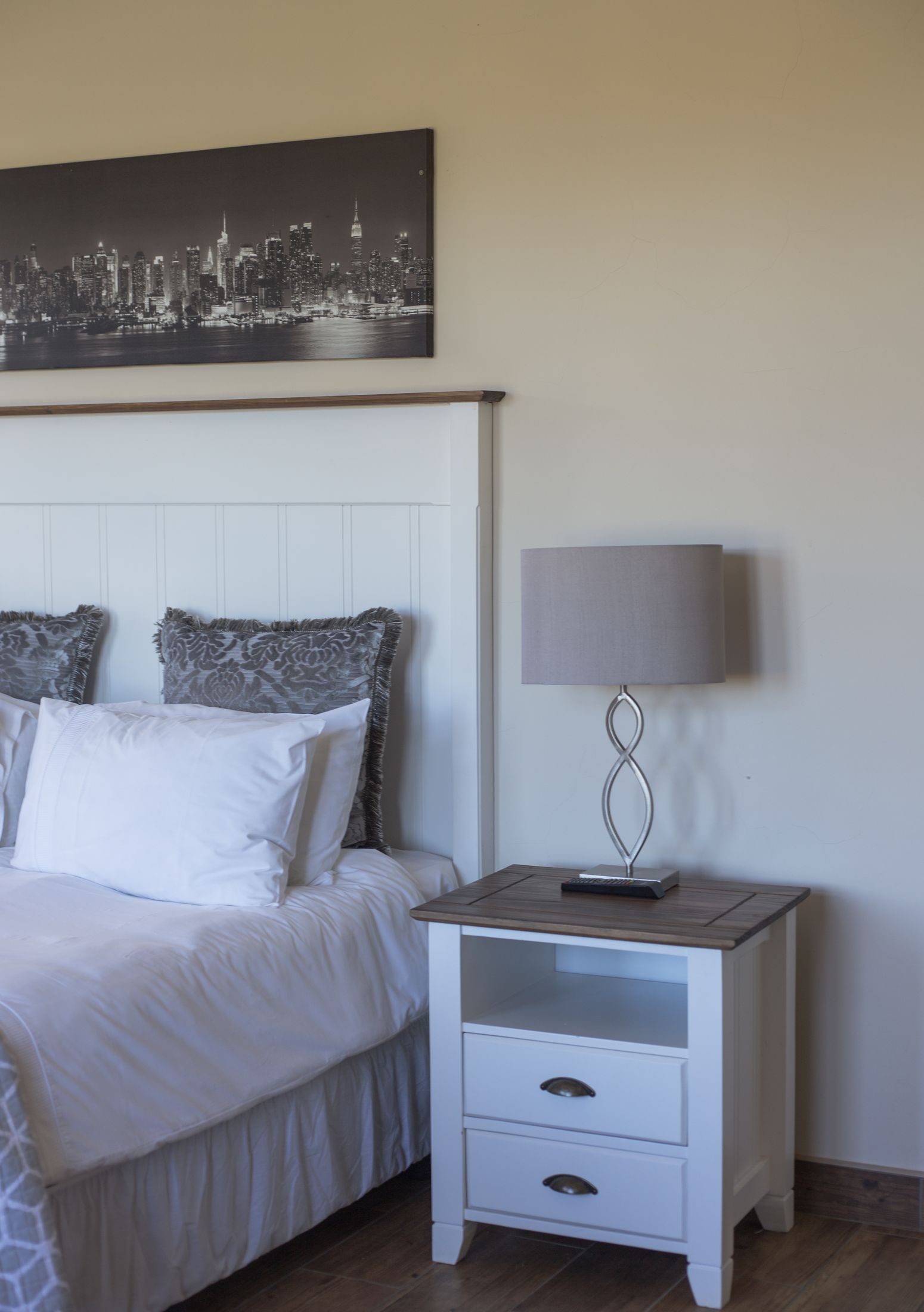 A bedroom with a white panelled headboard and a city print above the bed