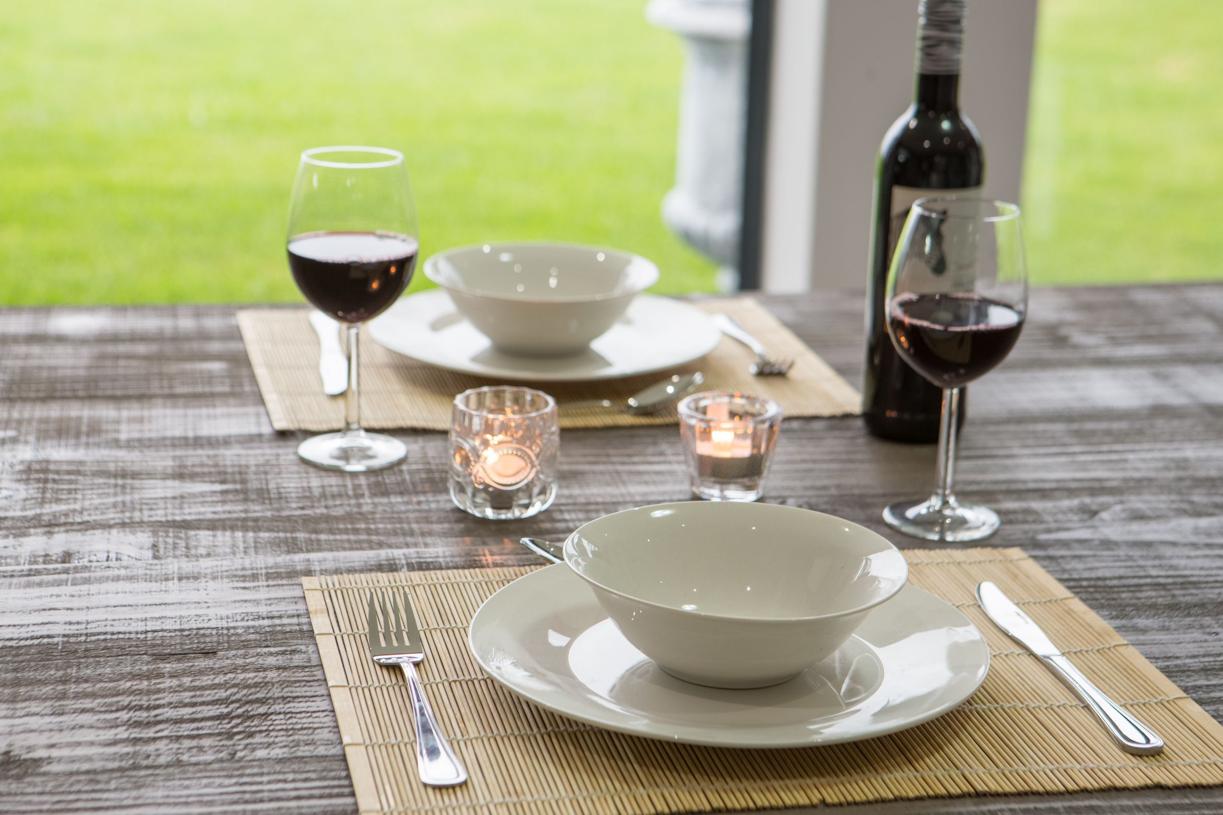 Bowls, wine glasses and candles set on the patio table, with the lawn behind