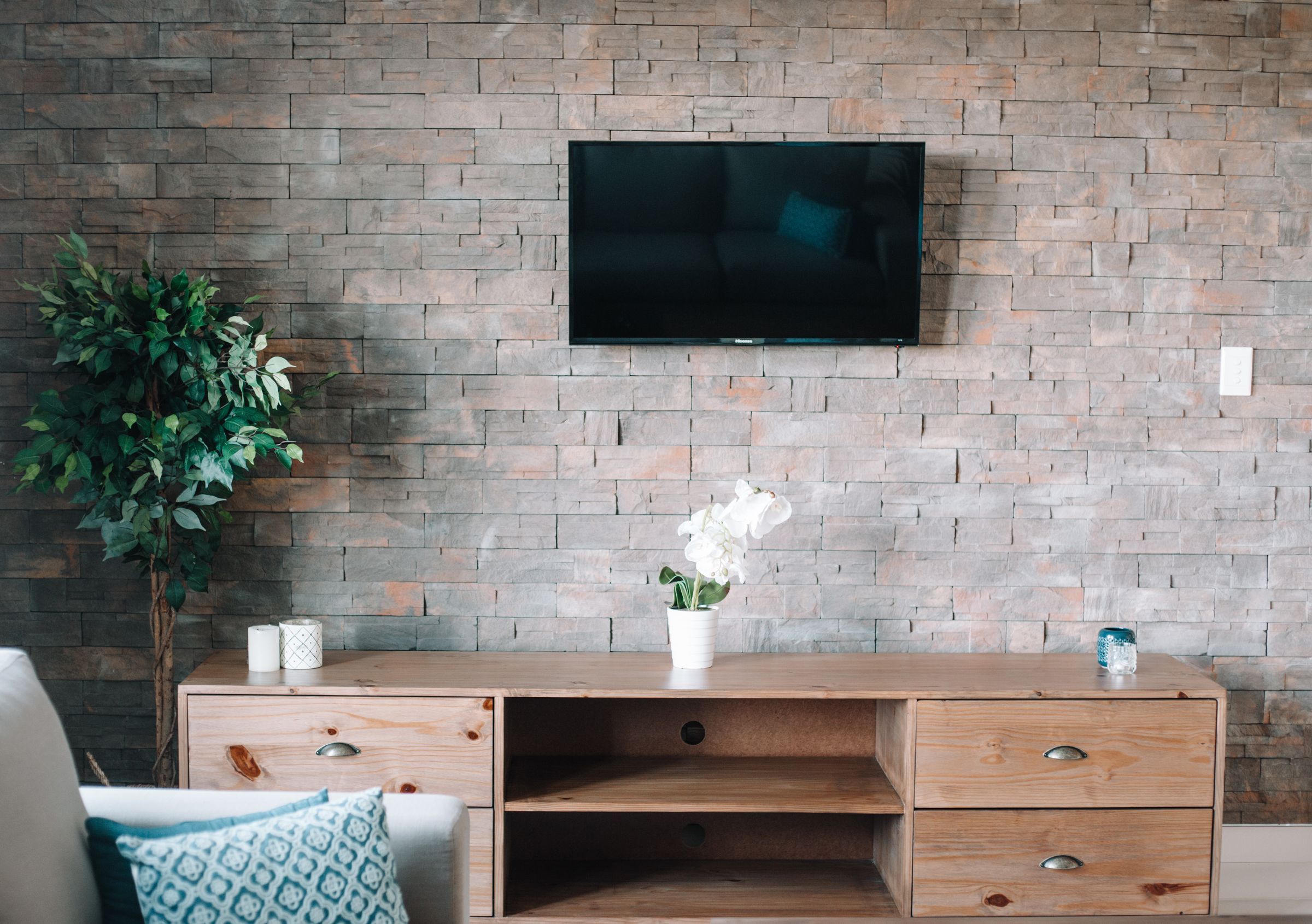 A timber TV cabinet and an orchid against the stone wall in the Unit 6 lounge