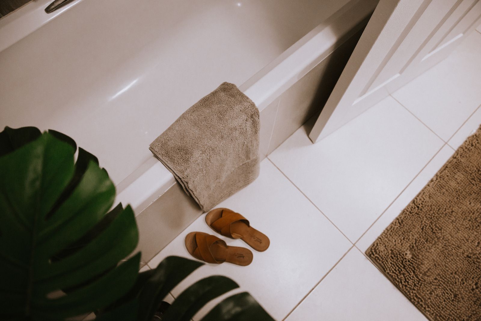A bath with a folded towel and slippers beside it