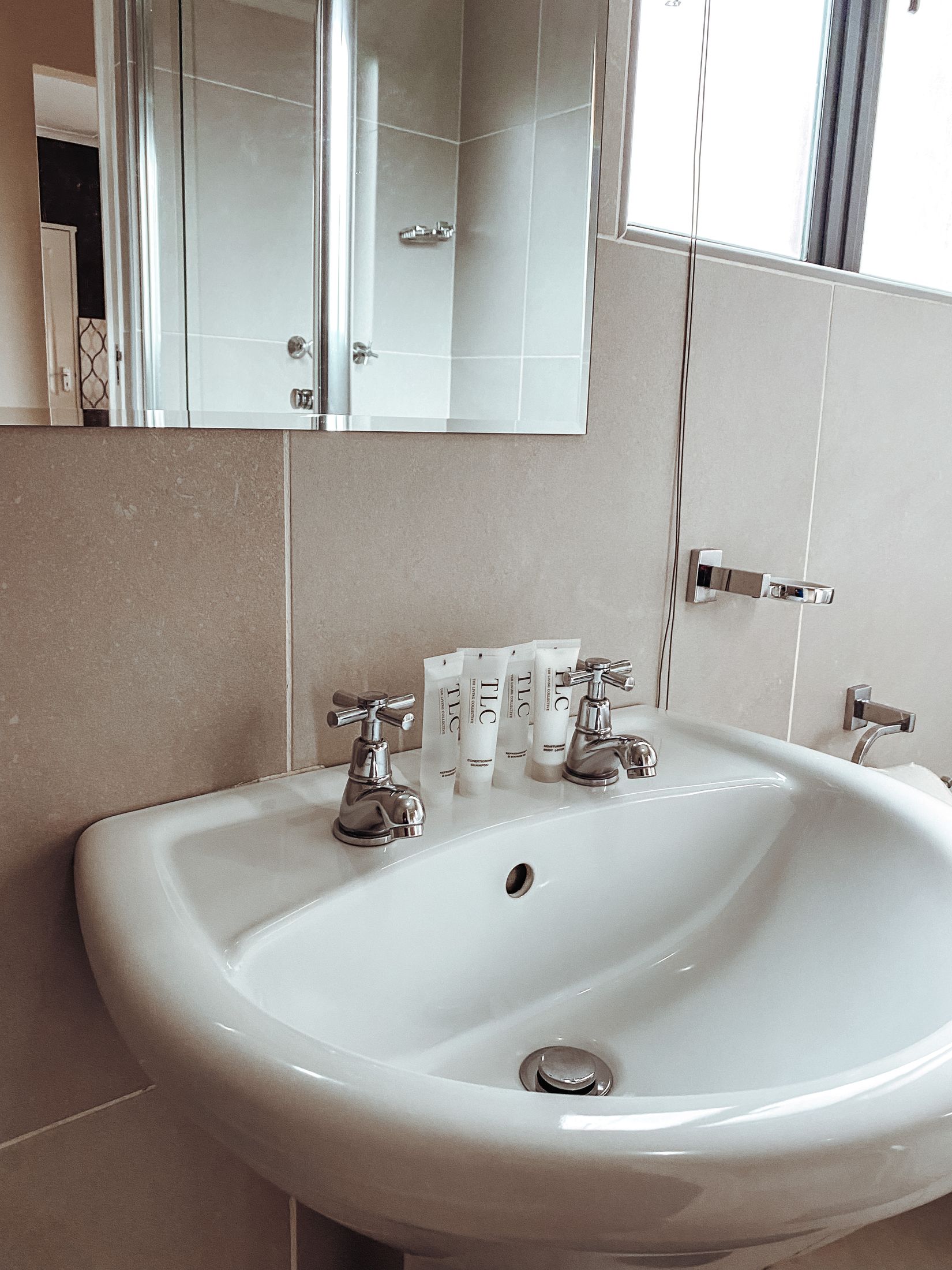 TLC toiletries on a white basin under the bathroom mirror