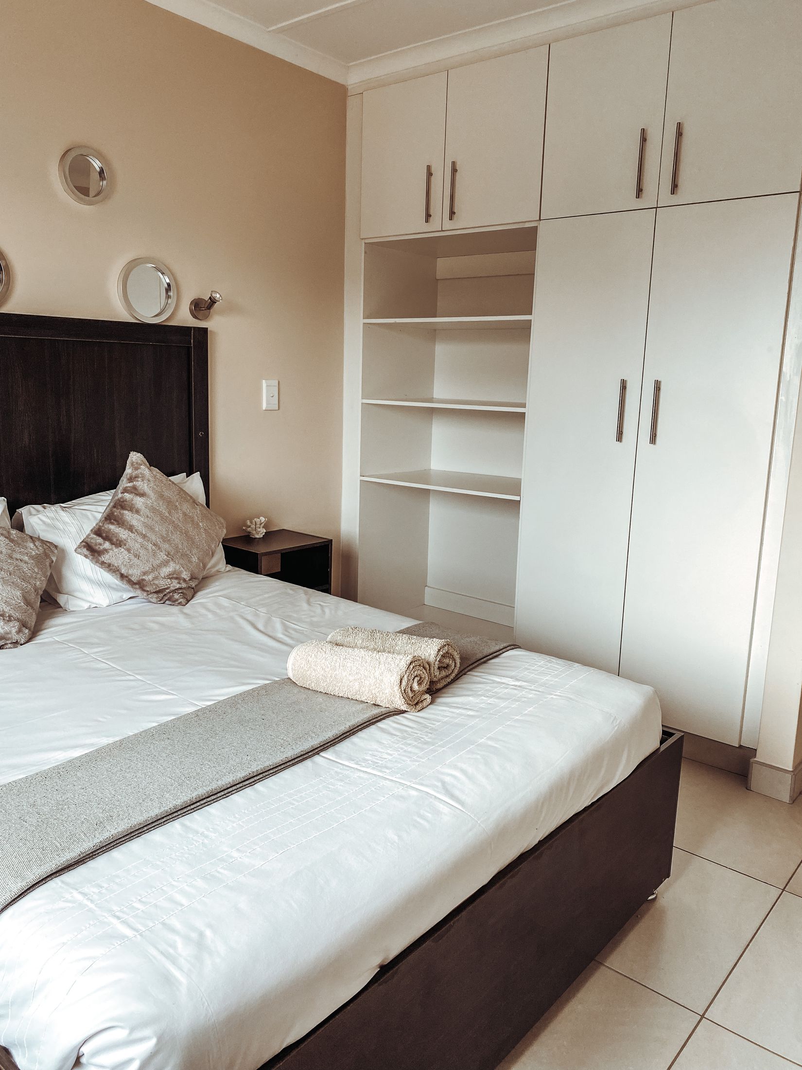 The bed beside built in white cupboards and open shelves