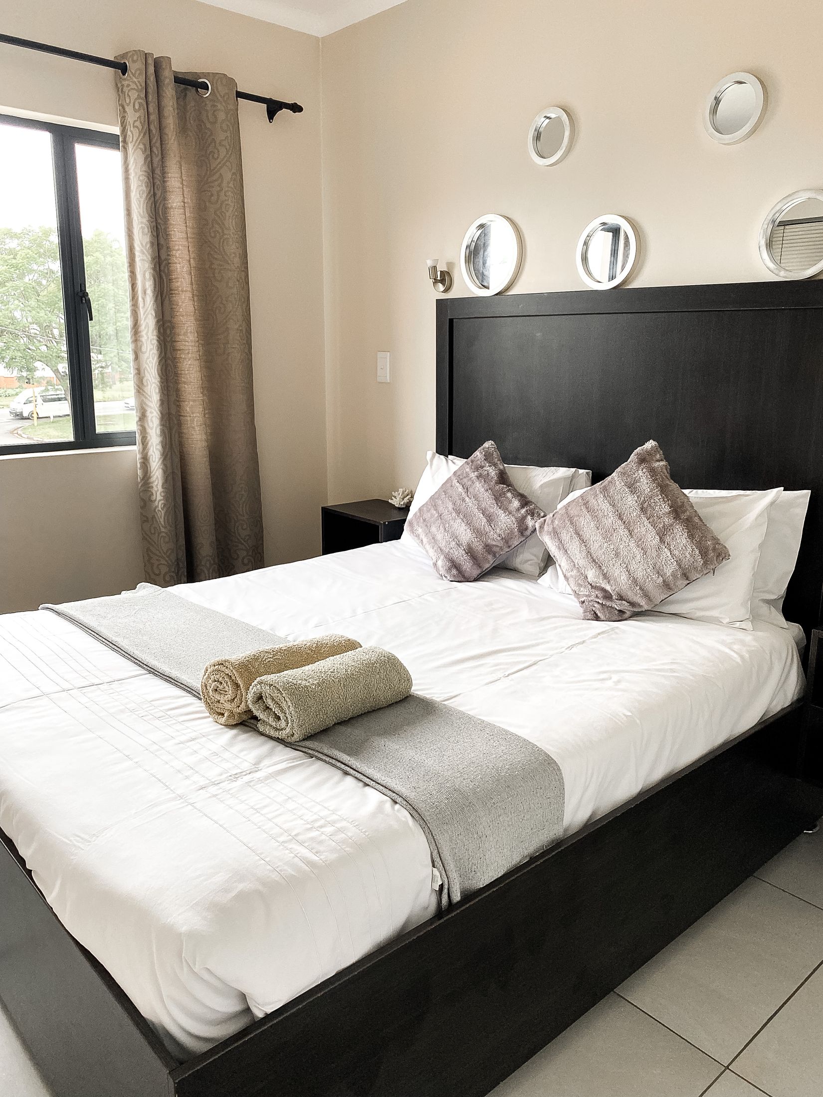 A double bed with a dark headboard, rolled towels and round mirrors above it