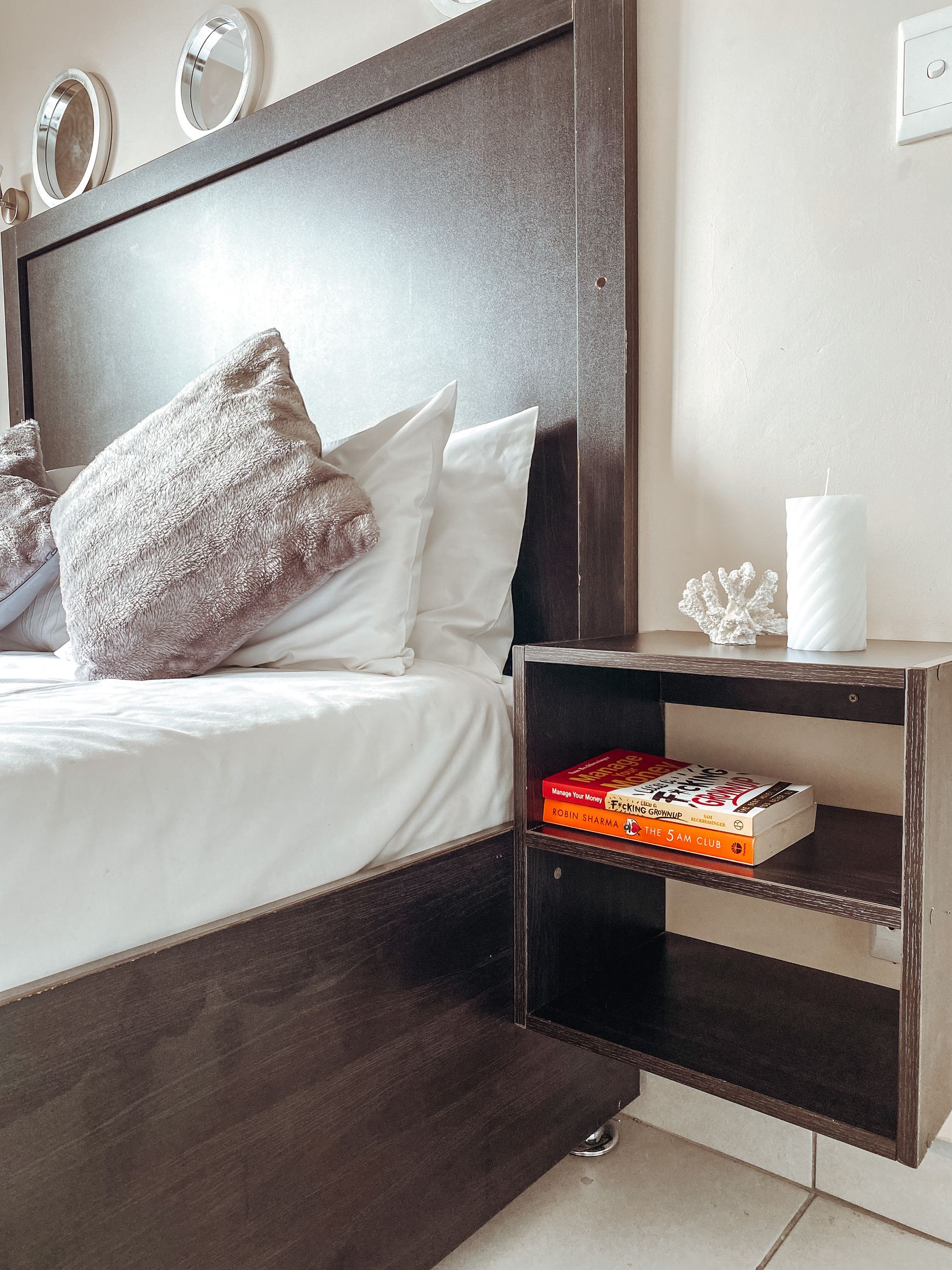 A bedside shelf with books and a candle next to the bed