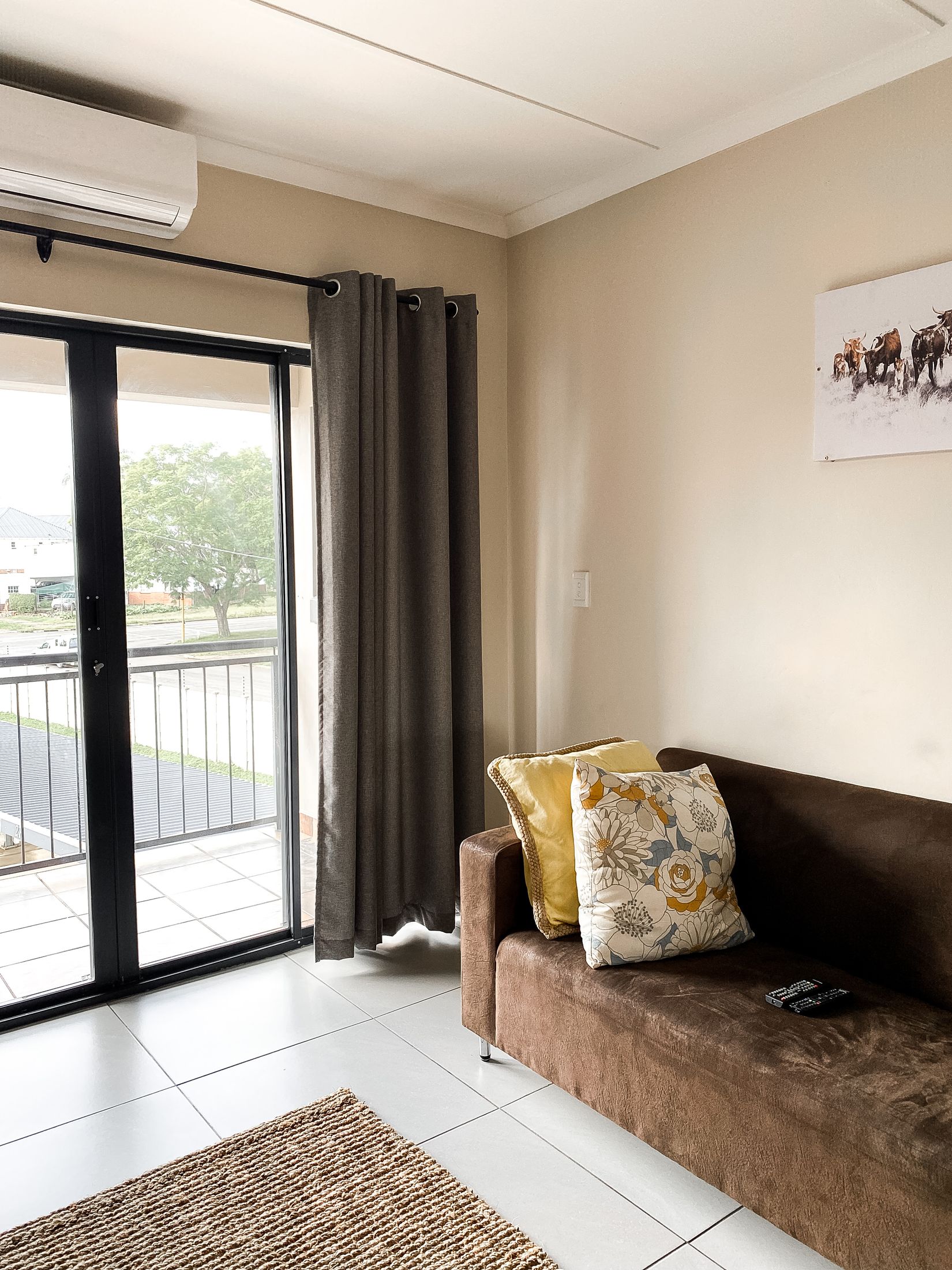 A brown couch with yellow cushions beside glass doors onto the balcony