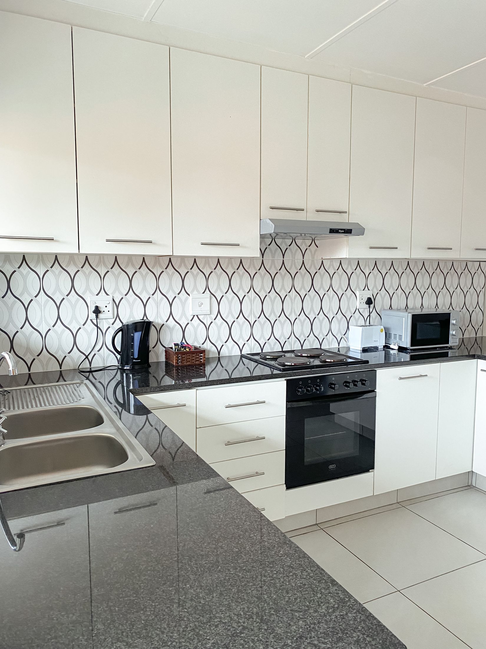 The white kitchen with patterned tiles, an oven and a double sink