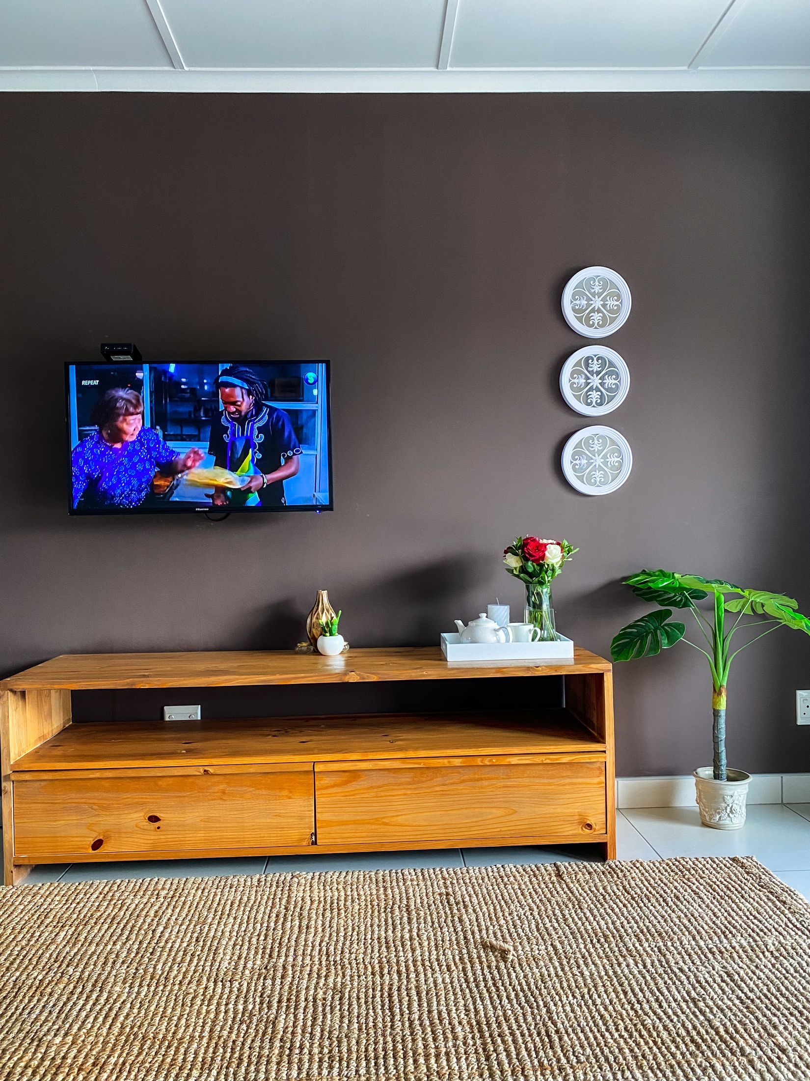 The lounge with a TV above a timber cabinet, white wall plates and a jute rug