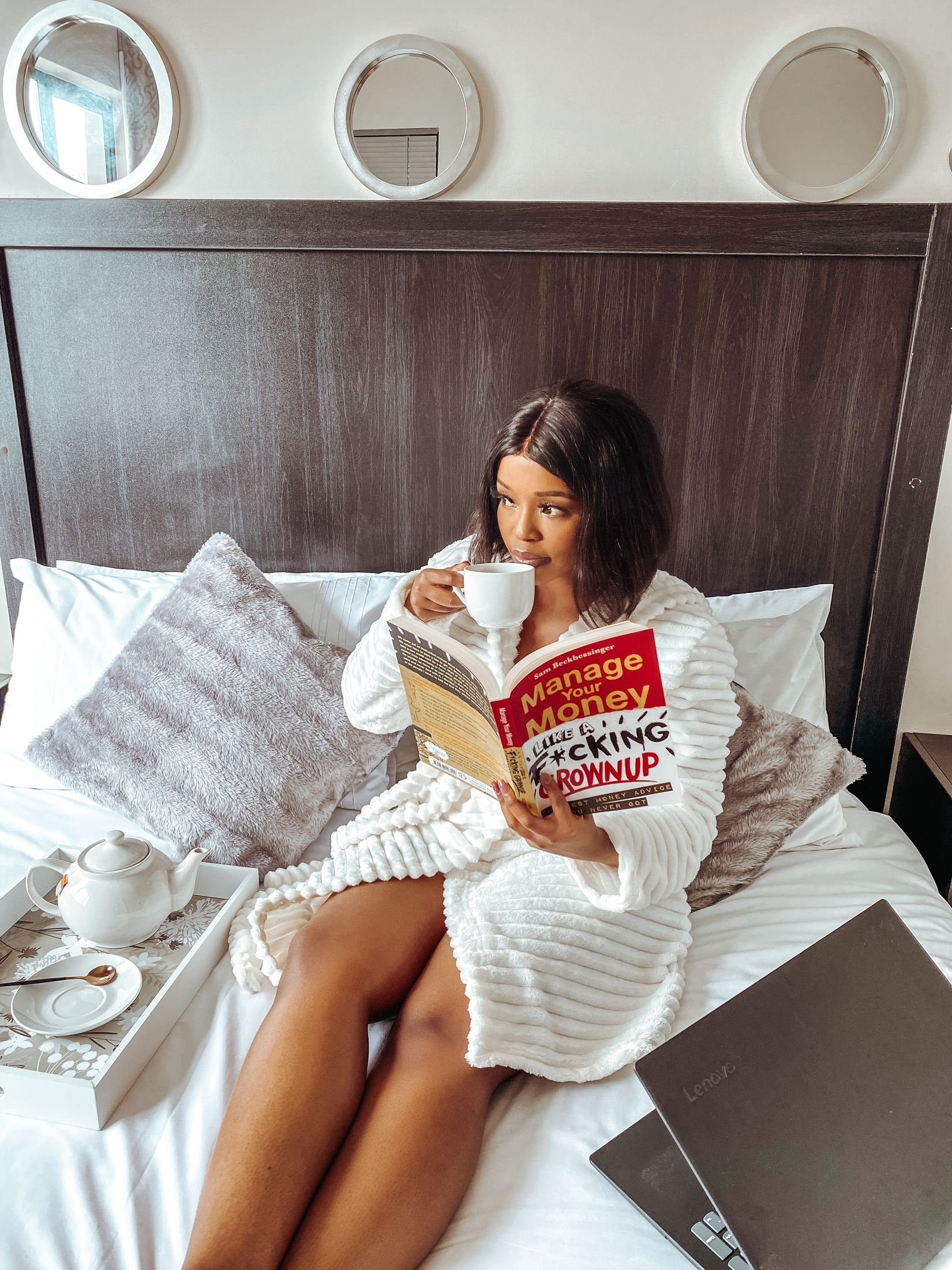 A guest in a white gown reading and drinking tea in bed