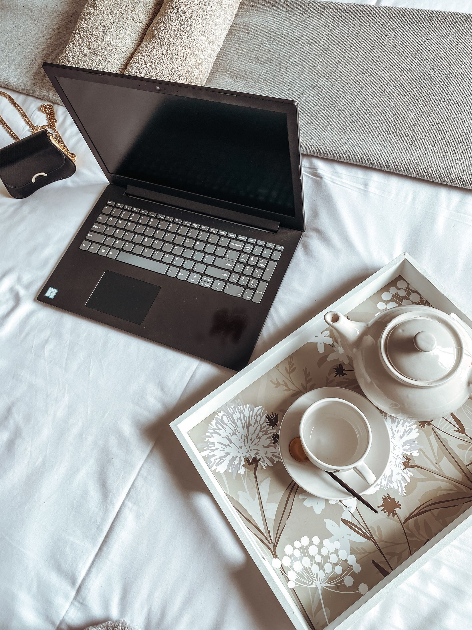 A laptop and a tea tray on the bed