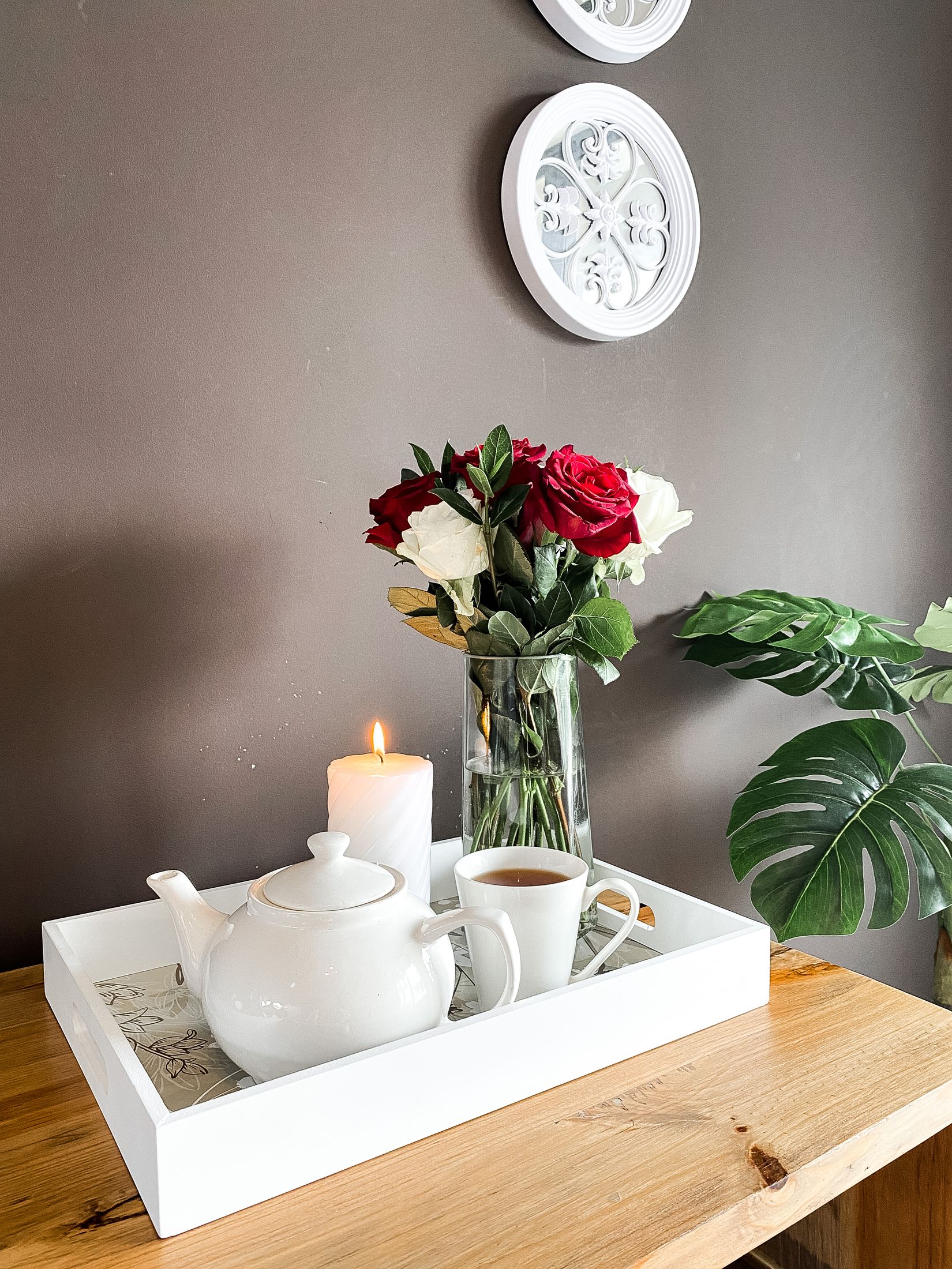 A teapot, a cup and a candle on a tray with roses behind