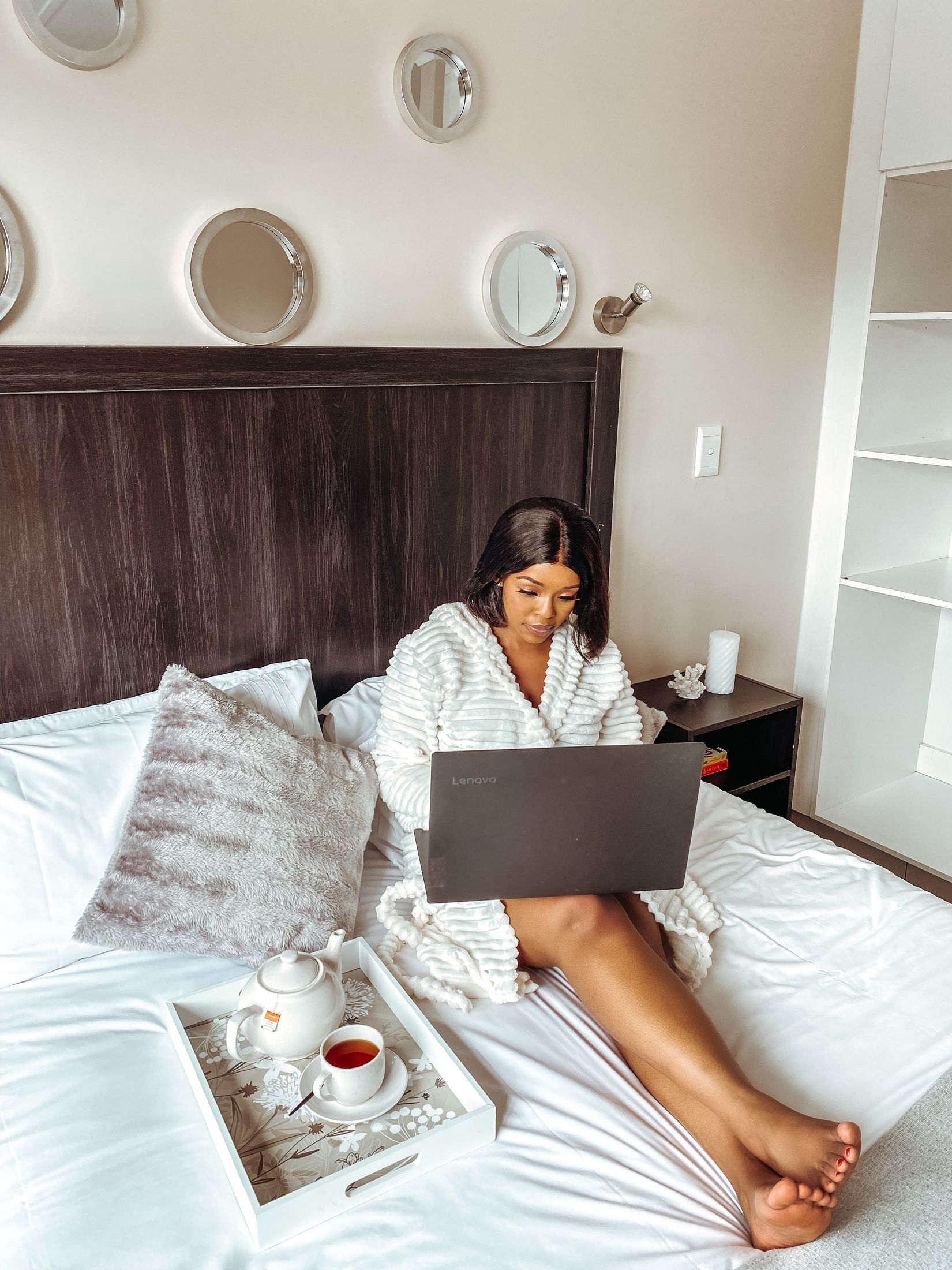 A guest working on a laptop in bed with a tea tray beside them