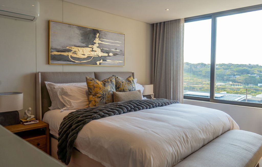 A bedroom with a wide window over the green coastal slope