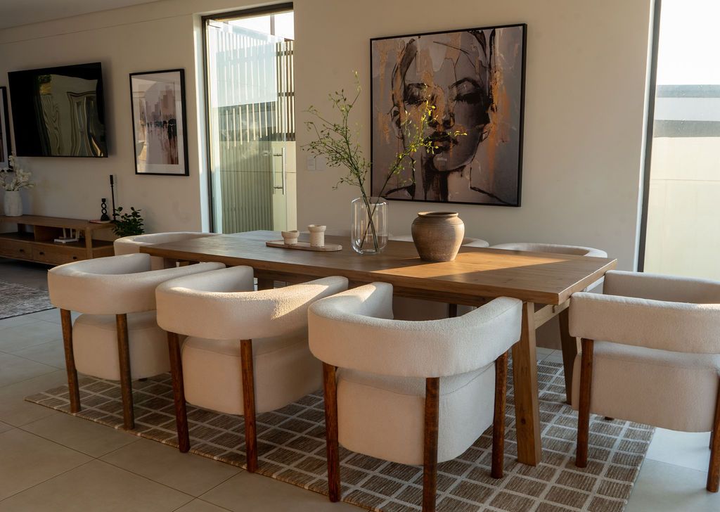 A dining table with curved white chairs under a large portrait print