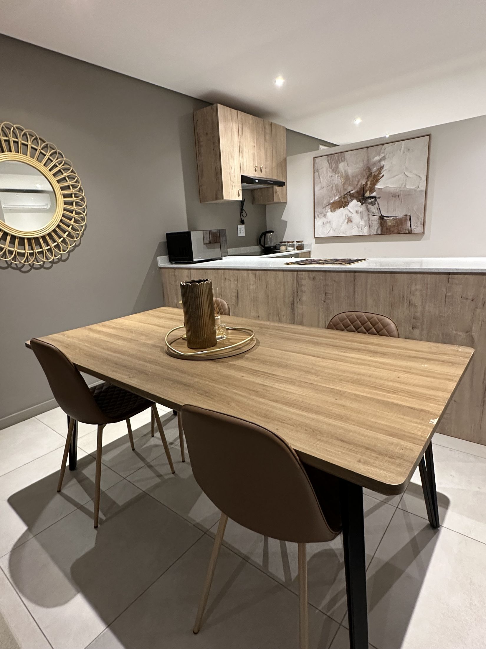 The dining table and the kitchen behind it, with timber cupboards and a framed print