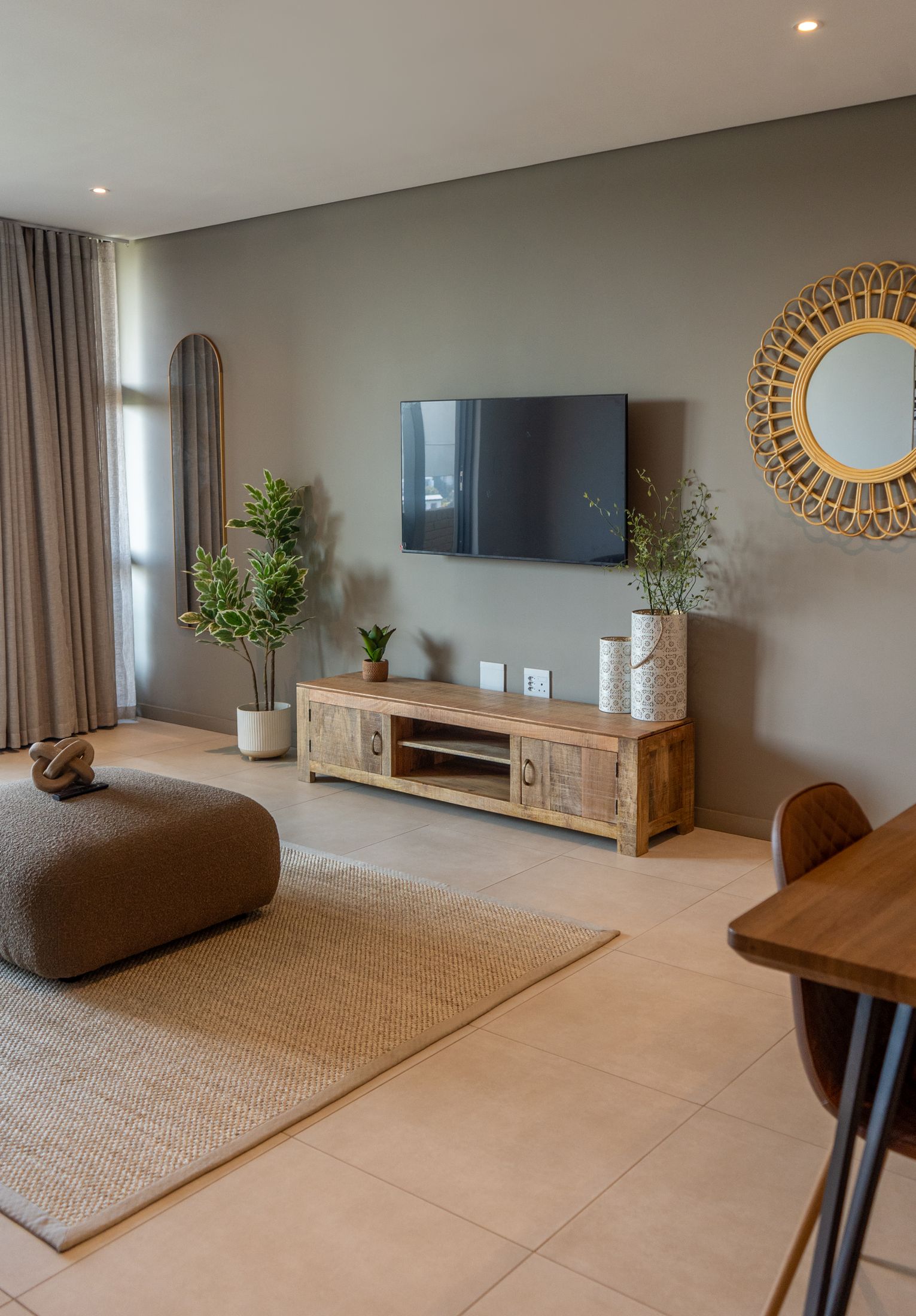 The loft lounge with a TV on a timber cabinet, a round rattan mirror and a jute rug