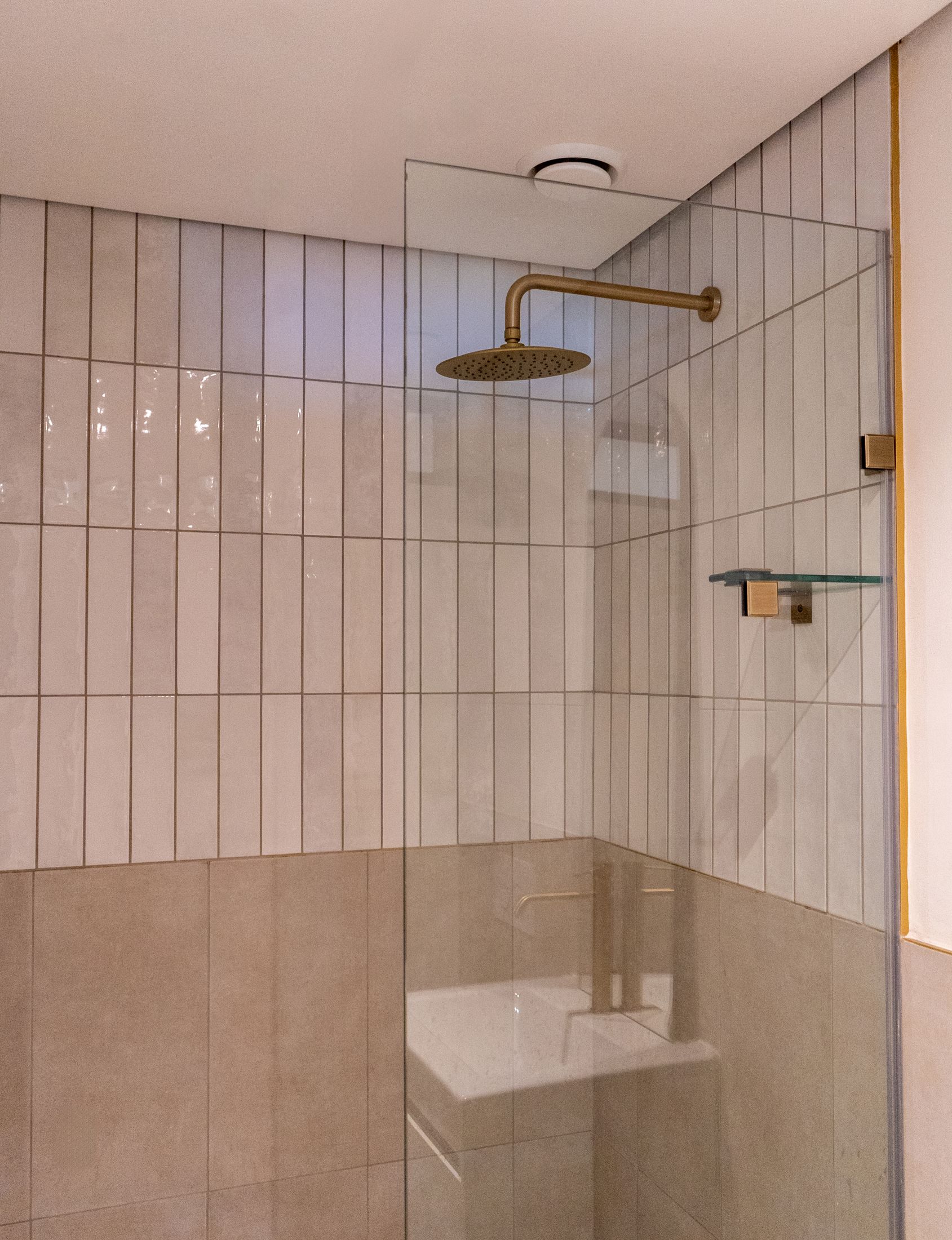 A glass shower with white tiles and a brass rain shower head